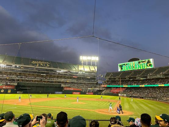 The Oakland Coliseum during an Athletics game. The stands are full and the big scoreboard says “Let’s Go Oakland”
