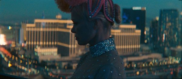 A dancer in costume stands in profile against a Vegas backdrop as the light fades in The Last Showgirl