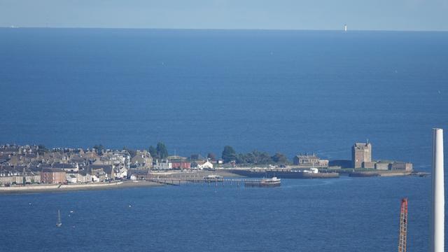 Hazy sunny view looking across blue River Tay towards Broughty Castle, and beyond that the North Sea and in the distance white Bell Rock Lighthouse