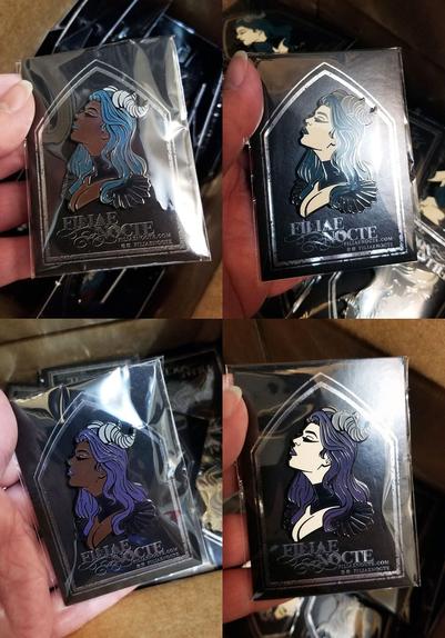 2x2 shots of all 4 regular editions of my first pin design. They're a bust of a fantasy pinup with horns and wavy hair, and she has a black collar and shoulder epaulets. The top two have teal hair, with a dark skintone on the left and a light skintone option on the right. The bottom two have lavender hair, with the same skintone options. All the pins are attached to cards bearing a silver foil tombstone and the company logo "Filiae Nocte" and are bagged in plastic sleeves.