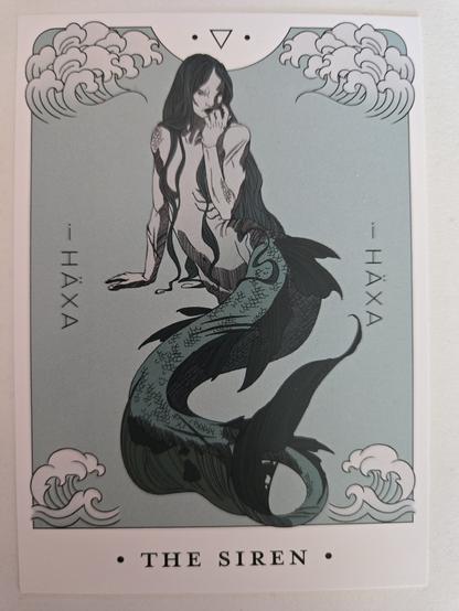 i Häxa's "Part Three" gatefold LP, paper card, showing the full picture of the siren from the vinyl in the same pose, but her fish-like green lower body is also shown. There are stylised waves next to her head and fin from both sides. The artist's name, i Häxa is printed vertically in both sides in the middle. The title of the card is below the picture: THE SIREN.