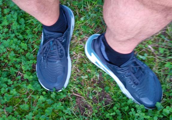 Auf dem Foto sind meine Füße und Unterschenkel in dunklen Laufschuhen zu sehen, auf einer Wiese. Bei den Schuhen handelt es sich um das Modell Altra Paradigm 7.