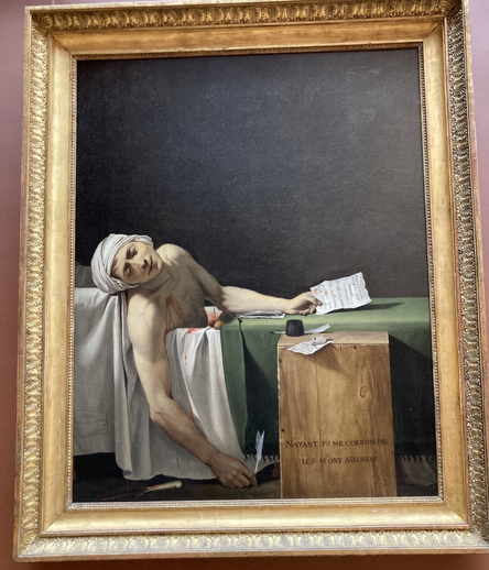 L’immagine ritrae il quadro “La morte di Marat” del pittore francese Jacques-Louis David in cui Marat giace senza vita, pugnalato a morte, sdraiato nella vasca nella quale passava la maggior parte della sua vita a causa della grave malattia che lo affliggeva.