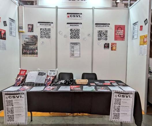 Foto del stand de CSVI. Tenemos panfletos, pegatinas del sindicato y QRs que enlazan a la encuesta y al fanzine, así como ejemplares físicos del fanzine.