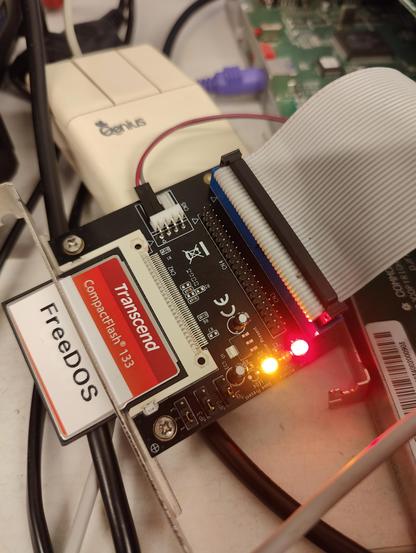 Photo of a CF-to-IDE adapter connected to a PC. A CompactFlash card with the label "FreeDOS" is mounted. LEDs are lit.