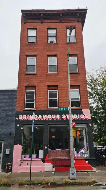 Photograoh of a tall rebrick 1800s town house with a store on thr ground floor. The storesign is colored allcaps designed as if each letter is a 3 layer cake with white on the top then red, then pink below