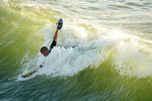 me with hands outstretched with hand planes on each, one hand down in the wave and the other above, riding the face of a breaking wave