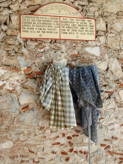 A notice, and a clothes line - with two wrap around skirts - hang on a stone and potsherd wall.