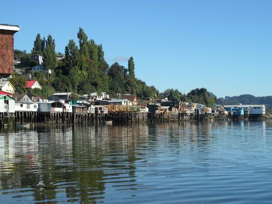 La vue des maisons sur pilotis annonce l'île de Chiloé au Chili. Le bord de mer se trouve juste en dessous des nombreuses maisons surélevées. Le ciel est du bleu des mers et océans.