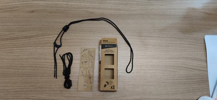 Unpacked set of quick laces from Decathlon. One lace is still bundled whereas the other one is folded open showing the two plastic stopper and locking pieces. There is a small cardboard set of instructions and also the small container in which it is packaged.