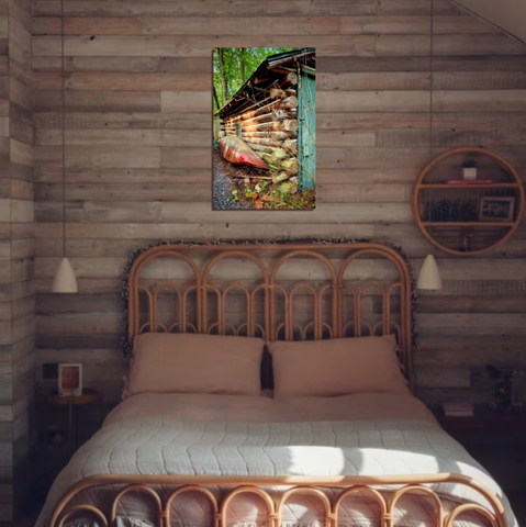 A red canoe leans against moss-covered log cabin, a striking contrast in greens and browns.