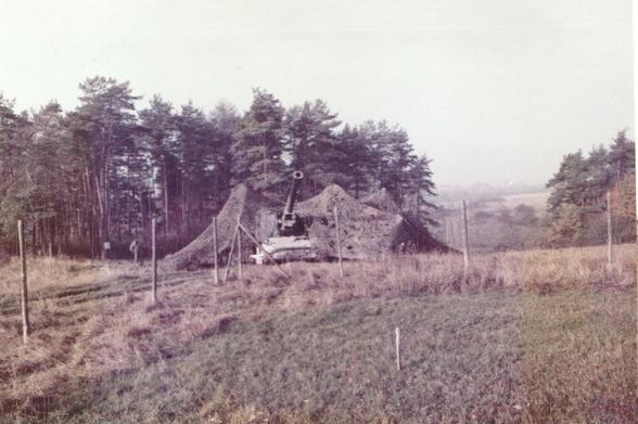 8-inch (203 mm) self-propelled howitzer and accompanying ammunition vehicle under a large camouflage net. Viewed from on the ground, maybe 100 to 200 meters away, the front of the cannon is still visible, but its shape was supposedly unclear from above.
