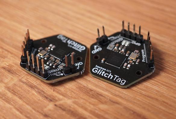 Two Glitchtag PCBs. Black hexagonal boards with GlitchTag text and pin headers.