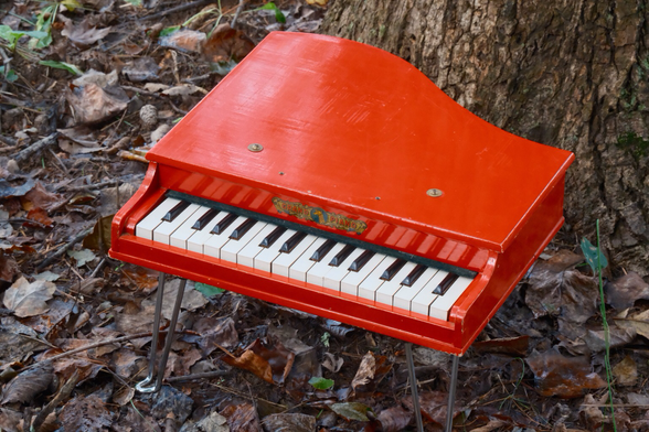 A grand piano outdoors. A toy grand piano to be precise, in all its glorious red paint, against a backdrop of nature
