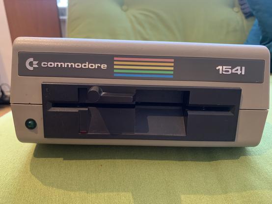 The front of a beige and dark brown Commodore 1541 floppy disk drive with C= logo and rainbow stripes.