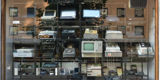 A photo through a store window of a display of cash registers/payment terminals on shelves.