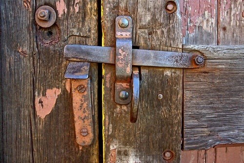Old train station roundhouse door handle close up. Rusted iron & steel lock & door handle mounted on wood. Rusty orange red patina peeling off.