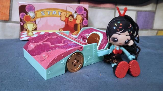 Ragdoll Vanellope sitting next to her race car. A small diorama of race starting line with a trophy and Wreck-It Ralph cheering is behind the car.