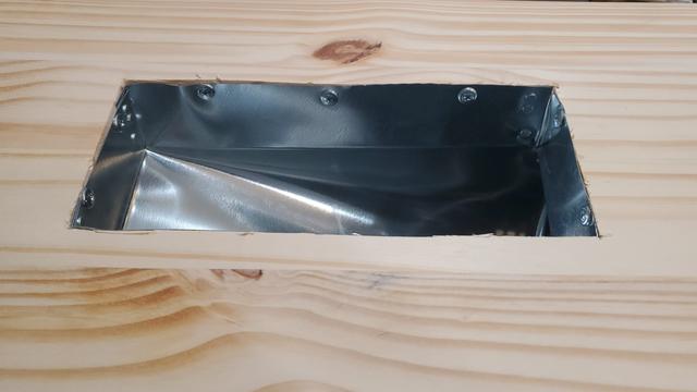 Outside view of an exhaust vent for a laser cutter\engrave, to be mounted in a window. Aluminum rectangular vent, screwed into a wooden board.