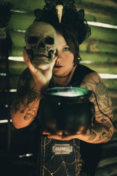Witch in a dark hut holding a skull over her right eye