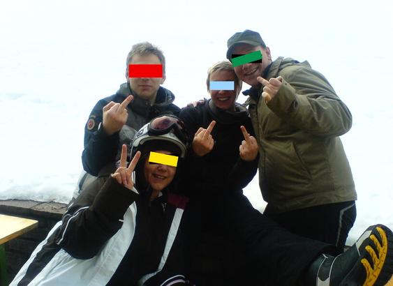 Farbfoto einer Gruppe von vier jüngeren Menschen bei einem Skiausflug in den Alpen. Sie posieren und machen dabei bekannte Fingerzeichen. Zum Schutz der Privatsphäre mit bunten Balken vor den Augen.