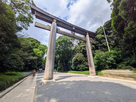 A large, unpainted torii gate with a gravel road going under it