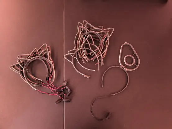 On the left: 6 pairs of 3d printed headbands with cat ears and led strips with an ESP32 C3 supermicro hanging from the side.

In the middle: 10 pairs of 3d printed headbands with cat ears and led strips with an integrated rudelblinken pcb.

On the right: 1 3d printed headband with an avocado instead of cat ears
