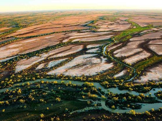 Aerial view of a sprawling, dry landscape with winding river channels and sparse vegetation, under a clear sky.
