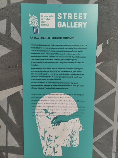 un cartel con el siguiente texto en catalán.

LA SALUT MENTAL I ELS SEUS ESTIGMES

Aquesta singular exposició, realitzada per estudiants del batxillerat artístic de
l'institut Gabriel Ferrater, ens submergeix en la complexitat de la salut mental
a través de les set obres d'aquesta exposició. Cada una reflecteix la visió
personal i colHectiva dels joves artistes sobre els estigmes que sovint
envolten la salut mental. Ubicades en l'històric edifici del Vapor Vell, aquestes
creacions conviden a la reflexió i al diàleg, desafiant percepcions
preconcebudes i promovent una major comprensió sobre aquest tema tan
important.

Aquesta exposició no només posa de manifest el talent dels nostres joves,
sinó que també evidencia el poder de l'art com a vehicle de canvi social i
conscienciació. Les obres a peu de carrer són invitació a connectar amb les
narratives personals darrere de cada peça i a participar en la construcció
d'una comunitat més inclusiva i conscient.