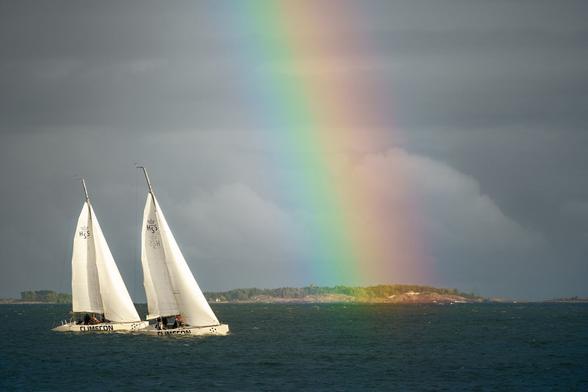 Two sailboats in a gulf under the rainbow sailing towards it