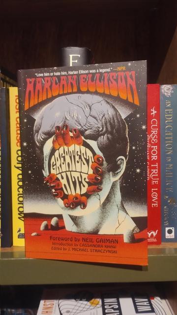 Cover to Harlan Ellison - Greatest Hits, curated by J.M Straczynski, published Union Square & Co, in front of one of the Science Fiction bookshelves in the Edinburgh Bookshop