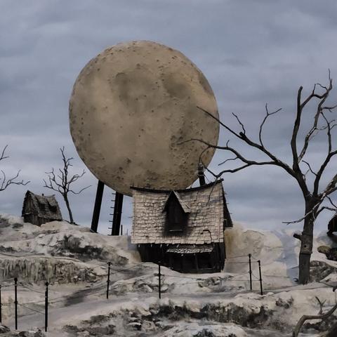 Teil der bühnendeko mit dem bleichen Mond. Davor ein Haus auf schneebedeckter Landschaft