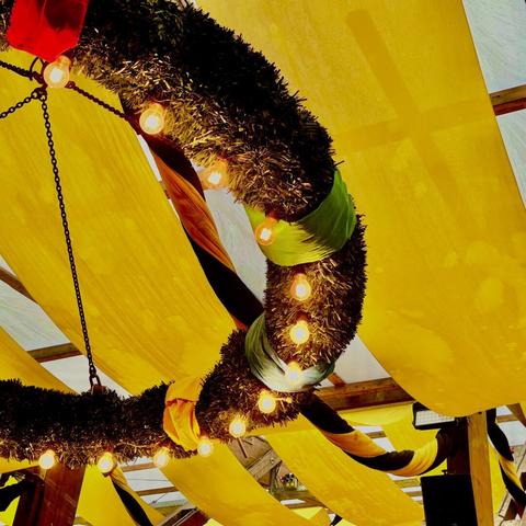 Zeltdach des Paulaner Festzelts. Gelbe Fahnen und ein großer Kranz mit Lichtern hängen von der Decke.