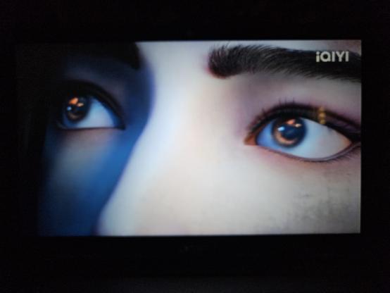 Extreme close up on two eyes looking sideways and up. The fighting celestials are reflecting as one red, one blue, and one yellow dot on his irises.