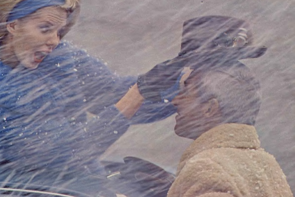 1962 

The image shows two individuals amidst heavy rain, with the backdrop of an overcast sky.
One appears to be shouting or reacting strongly while holding onto what seems like a part of their clothing, possibly due to being blown away by the wind.
Tags: stormy day, windy weather, emotional reaction
