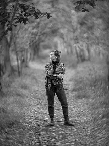 Portrait einer jungen Frau, die auf einem Waldweg steht, mit starkem swirly Bokeh um sie herum.