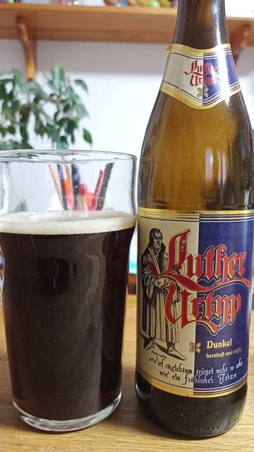 Auf einem Tisch steht ein Glas mit schwarzen Bier gefüllt und daneben eine Bierflasche