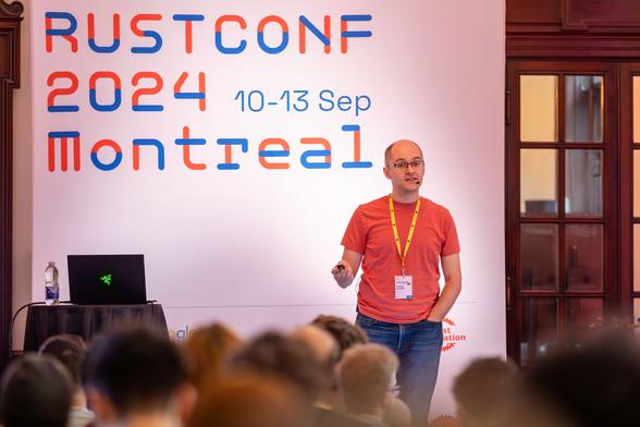 Predrag in the middle of his talk, standing in front of a giant "RustConf 2024, Montreal" banner.