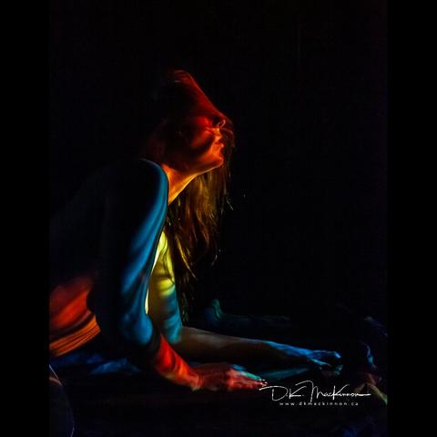 Woman with long hair covering their face as they look to image right, illuminated by a multi-coloured pattern.