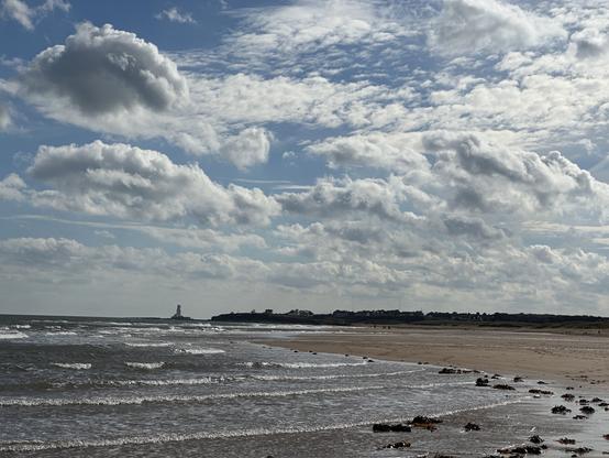A sandy beach under white and blue skies, with an obscured lighthouse in the far distance.