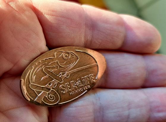 Auf meiner Hand liegt ein plattgewalztes und geprägtes 5 Cent Stück aus einem Andenkenautomaten. Es ist ein Chamäleon auf einem Ast sitzend eingeprägt und darunter der Schriftzug "Sea Life Hannover".