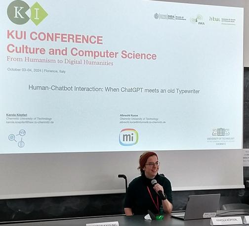 Bild zeigt lächelndeKarola bei der Präsentation des Papers Human Chatbot Interactions, when ChatGPT meets an old Typewriter auf der KUI Konferenz in Florenz mit der Startfolie des Vortrags im Hintergrund.