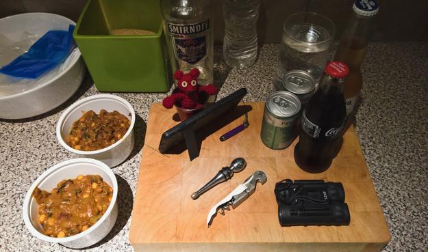 From #LeftToRight:

A #White #CeramicBowl containing an #Assortment of #ReusablePlasticBags;
#ChickPeaAndSpinachCurry #LeftOvers;
A #Green #CeramicBowl containing #Bread;
#CaptainRedBeanBear #TakingNotes on a #MicrosoftLumia950XL;
A #BottleOfVodka;
A #WineStopper;
A #BottleOpener;
#TwoCans of #ElderflowerFlavoured #TonicWater;
#OnePair of #Binoculars (8x21 #BinocularStrength)
A #Pint of #FreshlyChilledWater (#NotVodka);
A #SingleBottle of #Coke (without #Cocaine); and,
A #SingleBottle of #MexicanBeer.

#SomeItems are #Positioned on a #WoodenChoppingBoard and there is also a #BottleOfWater in #TheBackground set against a #Backdrop of #SpanishTiles 

If any #ALTTextNazis would like to #Translate #AllOfThis into: 

#Spanish;
#Dutch;
#French;
#Japanese; and,
#AmericanSignLanguage... 

Then #DoThat.