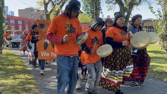Indigenous drummers marching in a park.