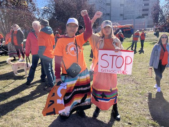 People wearing orange shirts posting with a sign saying Stop Genocide.
