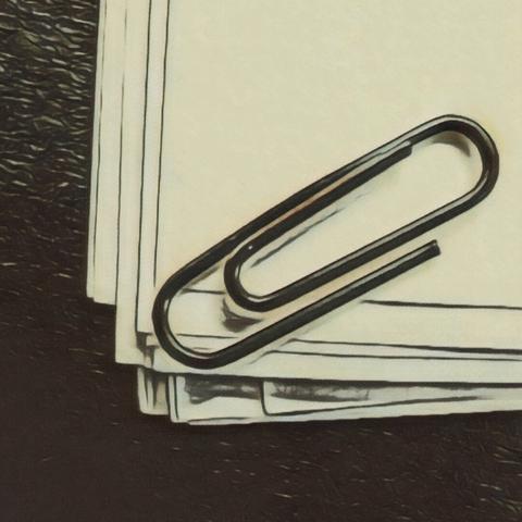 A stack of white papers and large paperclip positioned at the top right corner of the stack. The papers are slightly askew, The background is dark.