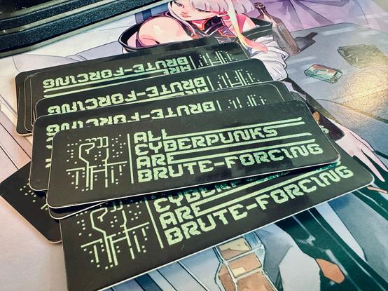 The image shows a stack of black stickers with green text and a digital-style fist graphic. The text reads "All Cyberpunks Are Brute-forcing."