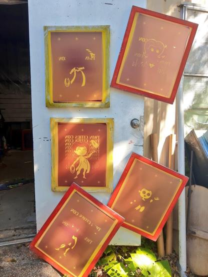 Five screens carefully hanging on a shop door, curing in the sun. Each screen showing a different layer of the artwork that will be printed onto apparel