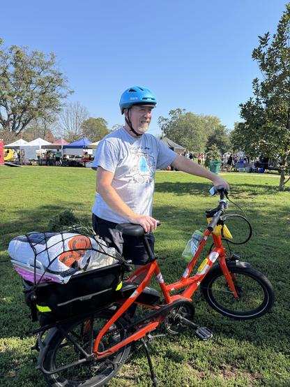 Person standing next to a cargo bike, with a farmers market in the background