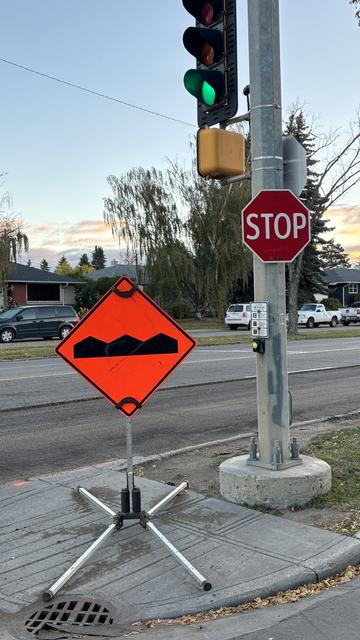 An orange bump warning sign placed on a small piece of sidewalk and blocking the pedestrian beg button at a crosswalk